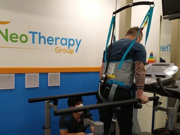 Physiotherapist helping man learn to walking on treadmill in a harness